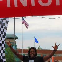 Torrey Thomas holding his hands high in the air, smiling wide, as he crosses the finish line